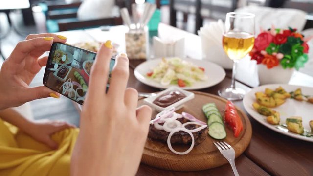 Food blogger hands using smartphone taking photo of beautiful beef steak on wood table inside the cafe to share on social media. Top view food photo. Lifistyle concept. Videoshot of people on vacation