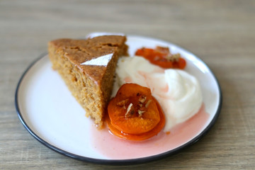 Slice of homemade sponge cake served on a table with whipped cream, cooked apricots and walnuts. Selective focus.