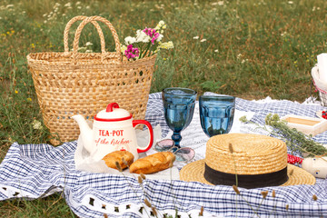 Stylish picnic on the green lawn. Fresh croissants and a teapot with tea on a bedspread near a wicker female hat. Instagram content