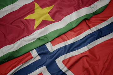 waving colorful flag of norway and national flag of suriname.