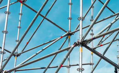 Fototapeta premium Metal pipe frame structure on blue sky background. Industrial construction from tubes raises upwards. Building process and joining elements view. Straight and inclined lines backdrop