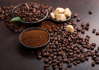 Fresh raw organic coffee beans with ground powder and cane sugar cubes with coffee trea leaf on brown background.