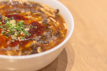 Close-up spicy Chinese hot and sour soup in white bowl in wooden table at the restaurants.