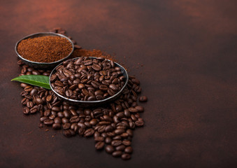 Fresh raw organic coffee beans with ground powder and coffee trea leaf on brown background.