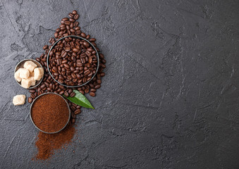 Fresh raw organic coffee beans with ground powder and cane sugar cubes with coffee trea leaf on black background.