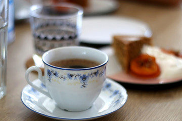 Cup of coffee and slice of homemade sponge cake served on a table with whipped cream, cooked apricots and walnuts. Selective focus.