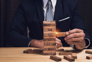 Asian businessman try to build wood block on wooden table at home office,business organization startup concept