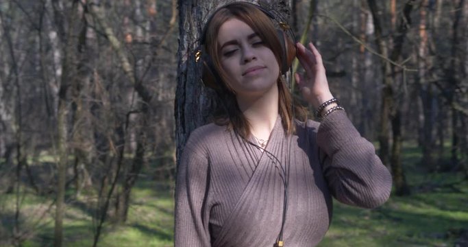 Beautiful young girl listening to music on headphones and enjoying the freedom and beauty of nature in the forest.