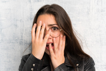 Teenager girl over grunge wall covering eyes and looking through fingers