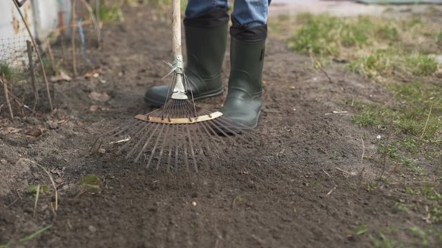 Gardener wearing rubber boots raking soil