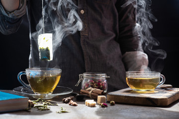 The steam from man with gray jecket is soaking tea bag on vintage white cup, preparing hot...