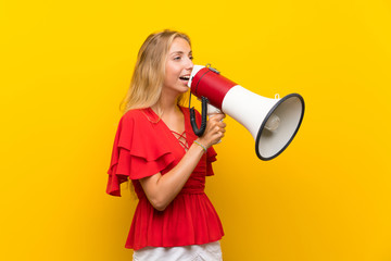 Blonde young woman over isolated yellow background shouting through a megaphone