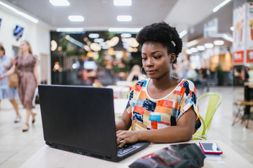 Beautiful Young Dark Skinned Freelancer Woman Using Laptop Computer Sitting At Cafe Table.  Freelance Work Concept.