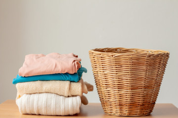 Wicker laundry basket with clean clothes on wood table against gray background. 