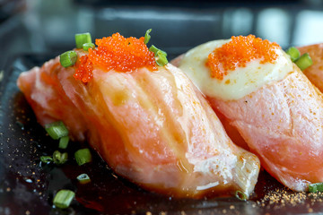 Closeup colorful Salmon Sushi with tobiko eggs on top in black plate on the black table background. Japanese Foods concept. Dark tone.
