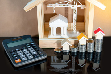 Banking concept. Loan interest rate calculation. Saving money for property investment or real estate development. Home mortgage and lease. Coin stacked, house and bank models with calculator on table.