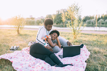 Dark skinned couple sitting on cover in autumn park and watching movie at laptop. Leisure and picnic concept.