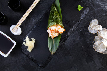 Close-up of tasty hand roll sushi with scaloop and Tobico caviar served on dark stone plate with soy sauce and ginger. Copy space. Temaki, Japanese cuisine. Healthy food. Seafood fish