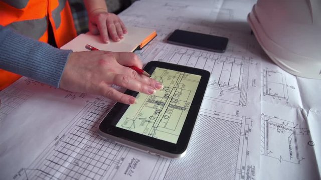 Woman architect uses tablet examining blueprints