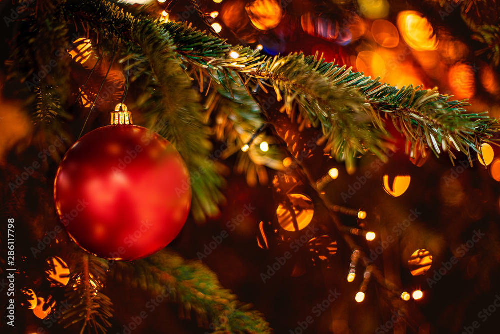 Wall mural decorated christmas tree on blurred background with golden sparkling bokeh lights and red ball. fest