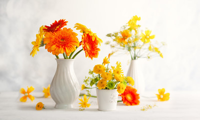 Beautiful bouquet of red and yellow flowers in white vase on wooden table, front view. Autumn still life with flowers.