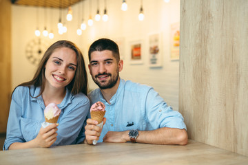 couple sitting and looking at the camera while eating ice cream indoor