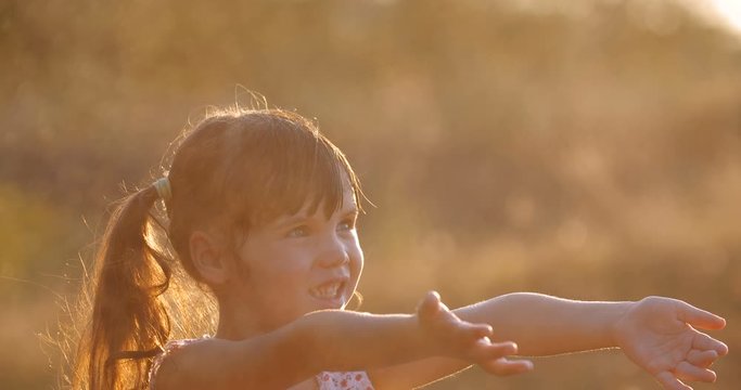 Close up little cute  girl  four  years old, having fun playing with splashes of water, jumping and catching in warm bright sunset rays  on a sunny summer evening. Slow motion 50 fps 4k 