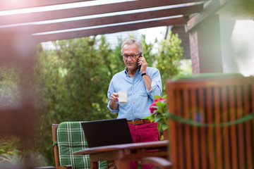 Fototapeta premium Senior man using mobile phone in backyard