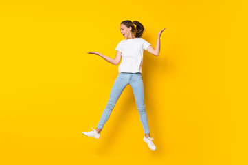 Fototapeta na wymiar Young woman jumping over isolated yellow wall