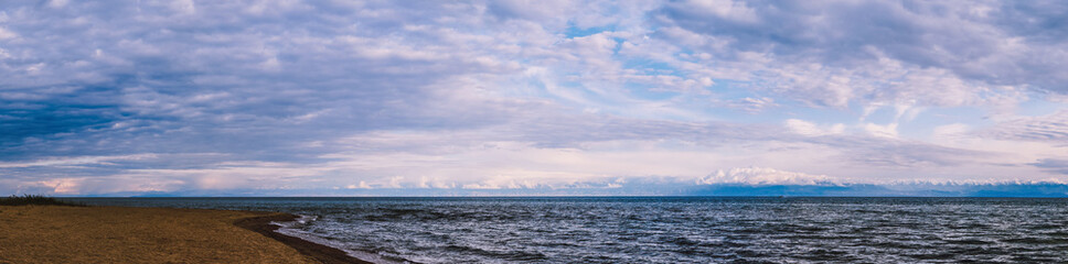 Beautiful panoramic view of the beach at sunset, illuminated by the evening sunlight against the backdrop of beautiful large mountains, luxurious summer adventures, outdoor activities, tourism