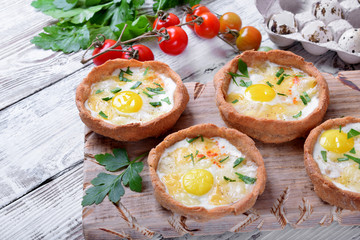 Baked rye tartlets with cheese and quail eggs on white wooden table