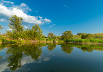 Blue sky, trees and clouds are reflected in the water.