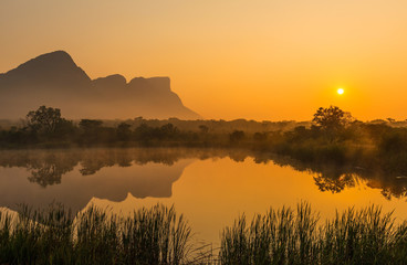 Landscape of the Hanging Lip or Hanglip mountain peak at sunrise with mist hanging above a swamp lake inside the Entabeni Safari Game Reserve, Limpopo Province, South Africa. - obrazy, fototapety, plakaty