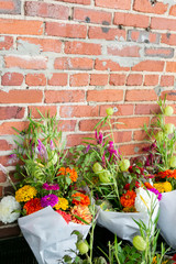 Fototapeta na wymiar group of colorful flower bouquets at farmers market, wild flower bouquets wrapped in paper, brick background