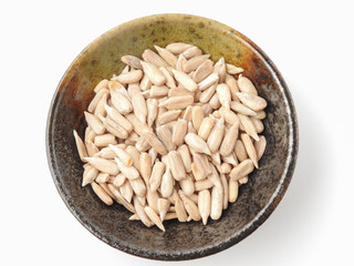 Top view of natural shelled organic sunflower seeds on pottery plate isolated on white background. It often eaten as a snack.  The seeds contain vitamin E. Food and snack concept. With copy space.