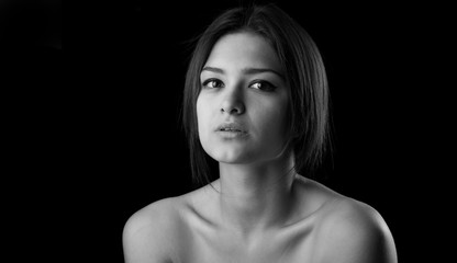 Dramatic black and white portrait of a beautiful lonely girl with freckles isolated on a dark background in studio shot