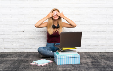 Teenager girl sitting on the floor with her laptop covering eyes by hands