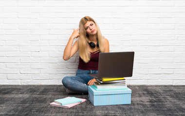 Teenager girl sitting on the floor with her laptop making the gesture of madness putting finger on...