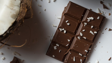 Confectionery concept. Chopped Coconut and pieces of dark chocolate on a white background, coconut flakes and deep shadows. Dessert recipe
