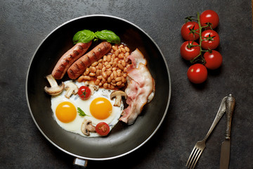 English breakfast. Fried eggs, sausages, bacon, beans, toasts, tomatoes on stone table. Top view with copy space