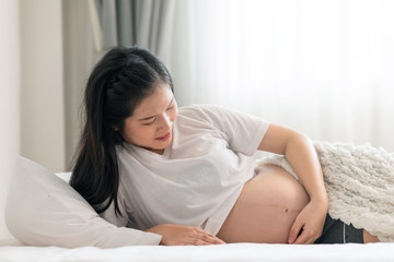 Asian pregnant woman laying in bed with open shirt. Touching her belly. With light leaks effect.