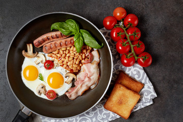 English breakfast. Fried eggs, sausages, bacon, beans, toasts, tomatoes on stone table. Top view with copy space