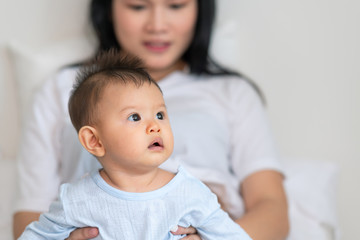 Asian male toddler sitting with his pregnant mother in bedroom. Curious look.