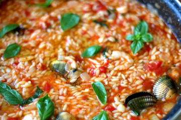 Orzo pasta, cooked with tomato sauce, vegetables and seafood, served on a table. Selective focus.