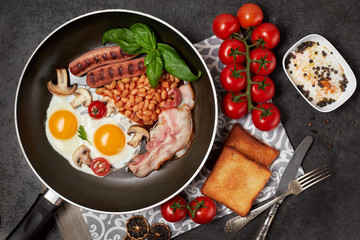 English breakfast. Fried eggs, sausages, bacon, beans, toasts, tomatoes on stone table. Top view with copy space