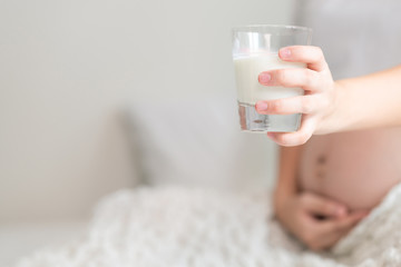 Asian pregnant woman holding a glass of milk in bedroom. With copy space. Side shot focus on milk.