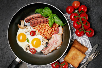 English breakfast. Fried eggs, sausages, bacon, beans, toasts, tomatoes on stone table. Top view with copy space