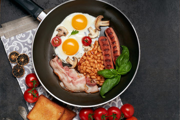 English breakfast. Fried eggs, sausages, bacon, beans, toasts, tomatoes on stone table. Top view with copy space