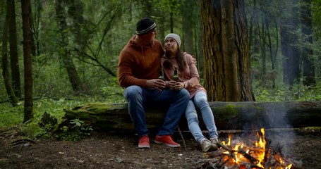 loving spouses are embracing warming by campfire in forest