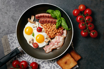 English breakfast. Fried eggs, sausages, bacon, beans, toasts, tomatoes on stone table. Top view with copy space